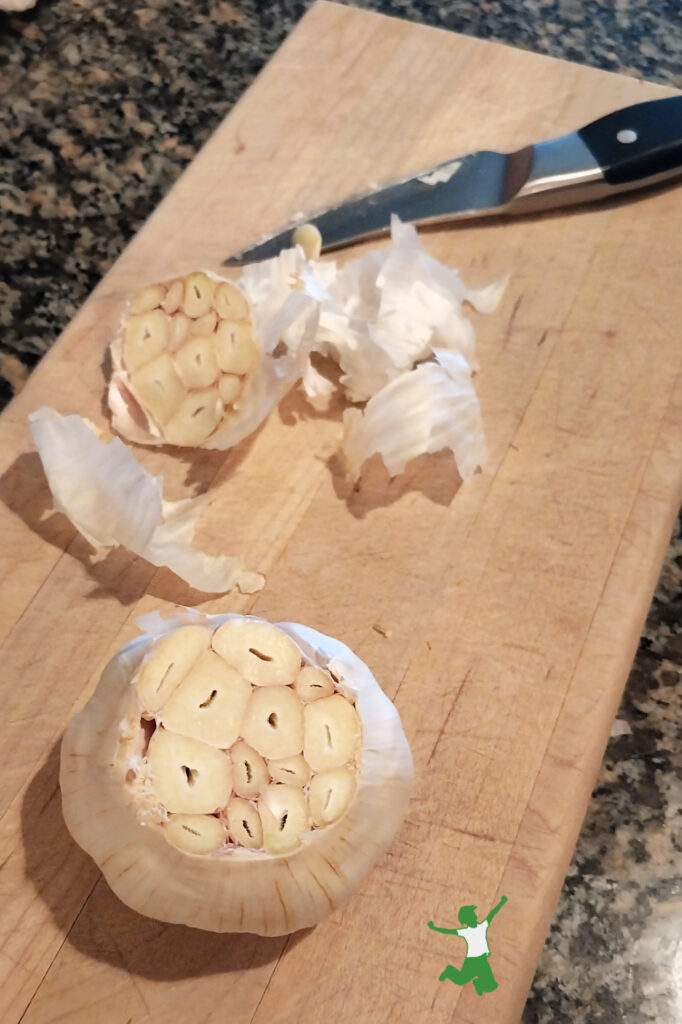 garlic head on cutting board with top removed for roasting